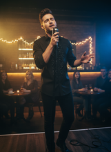 Man singing into a microphone on a stage with a dark, cozy ambiance